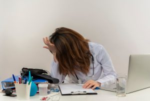 Stressed female doctor wearing medical robe and stethoscope, with medical tools on her table.
