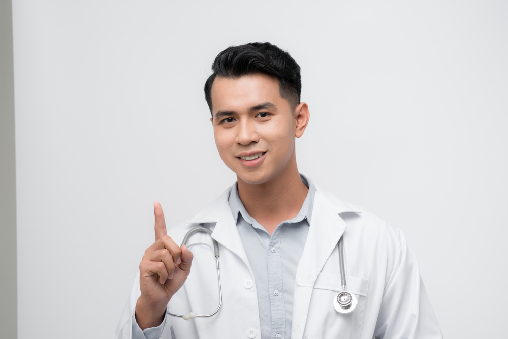 A filipino virtual assistant work ethics doctor is smiling and making a hand sign to show loyalty to his company.