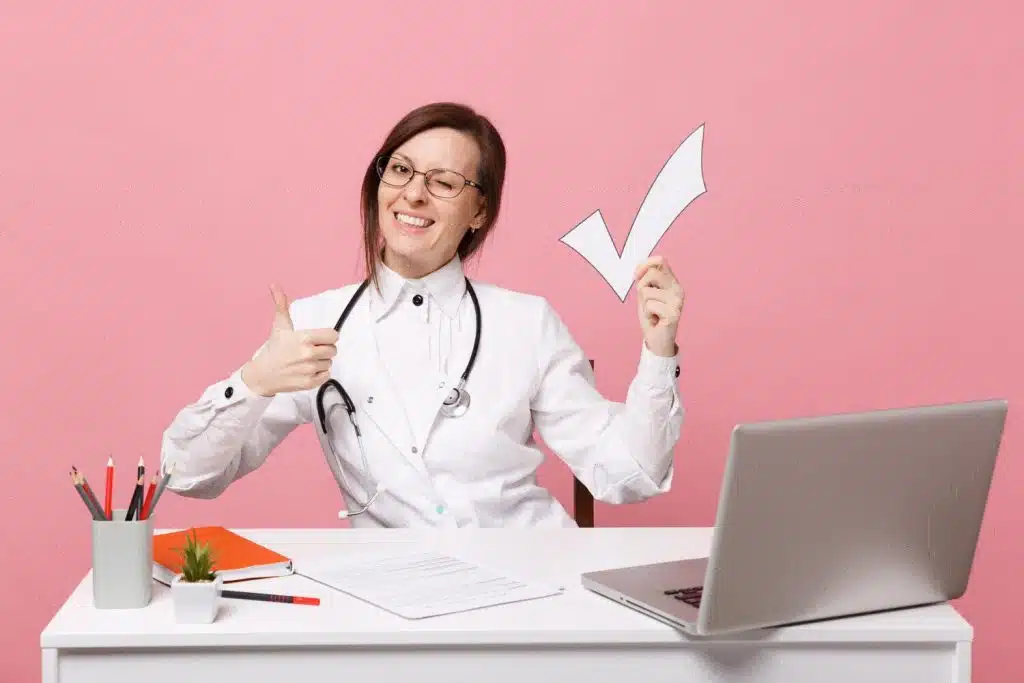 A growth oriented medical receptionist working on computer ,wearing glasses, smiling.