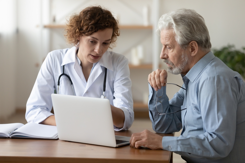 Doctor consulting a patient during an appointment, explaining and showing medical checkup results on a laptop screen.