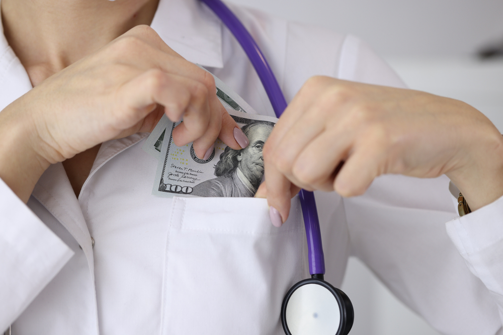 Doctor puting dollar bill in uniform pocket 