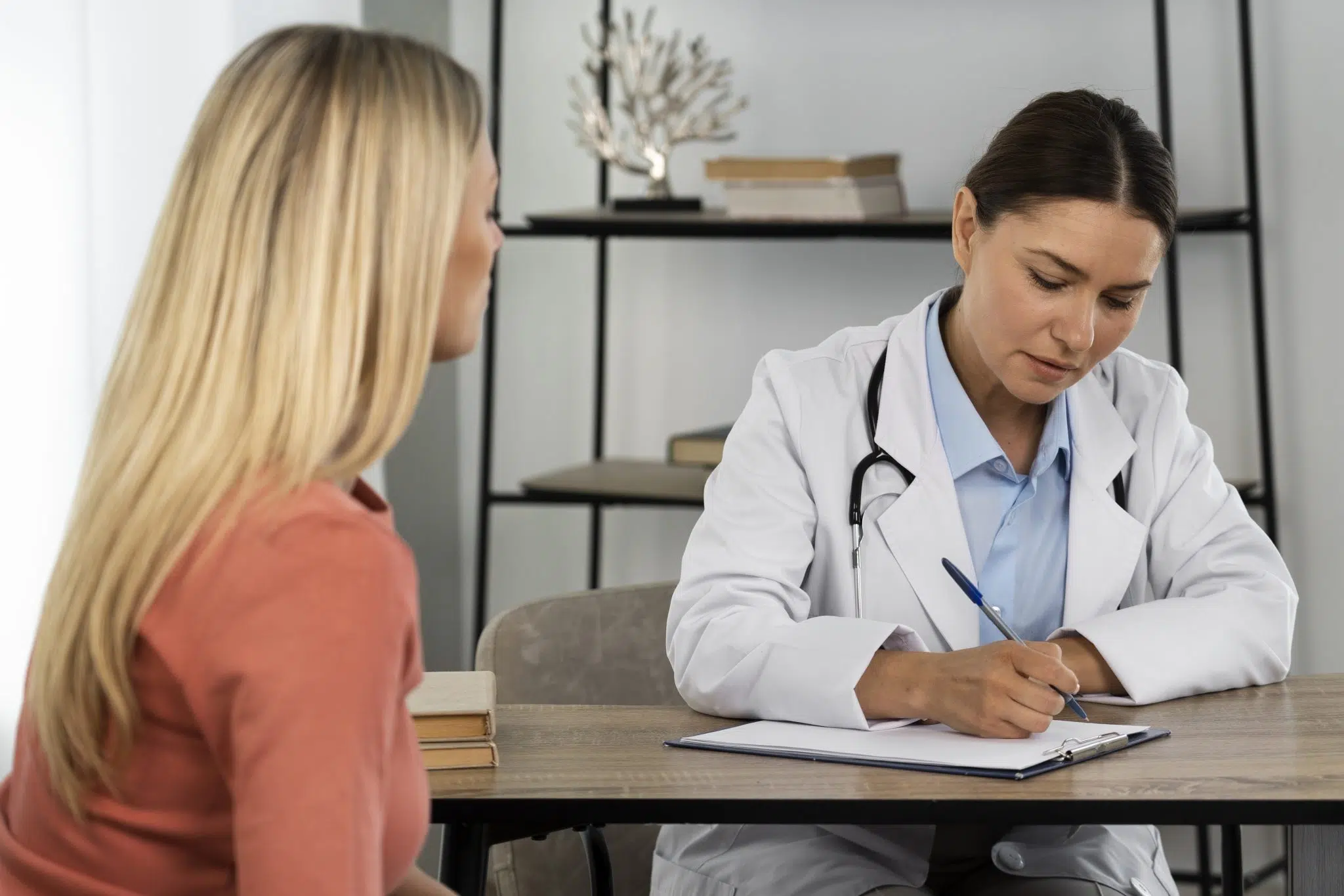 A medical professional typing notes while speaking with a patient, representing a medical virtual scribe