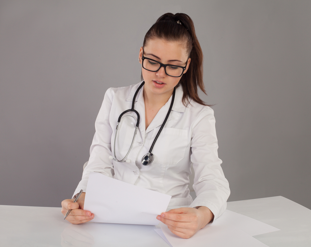 A medical virtual scribe in a robe and stethoscope documents patient information.