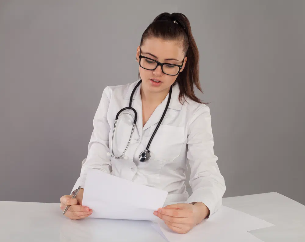 A medical virtual scribe in a robe and stethoscope documents patient information.