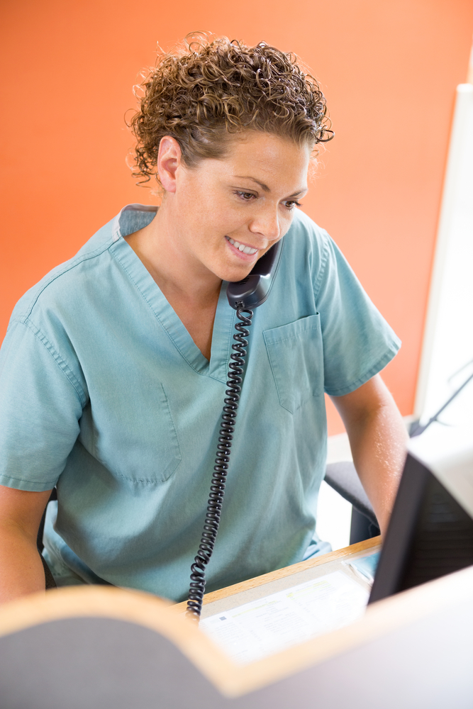 Busy medical receptionist answering telephone while working.