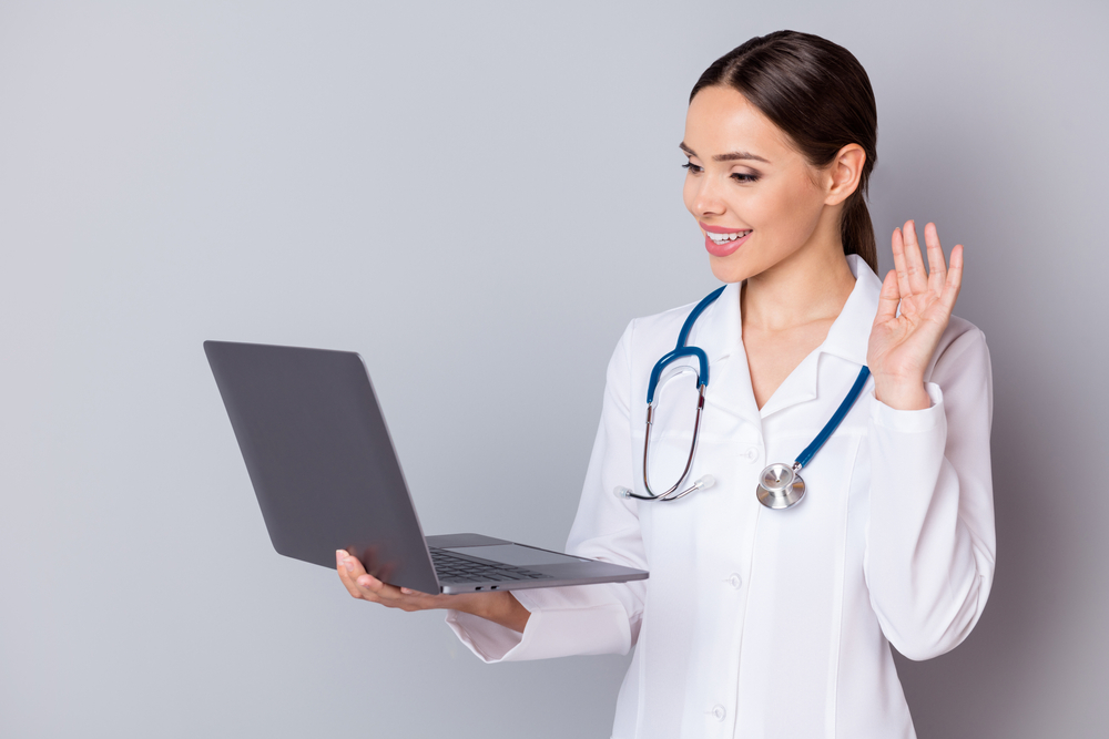 Female medical virtual assistant holding a laptop talking a patient through a videocall.