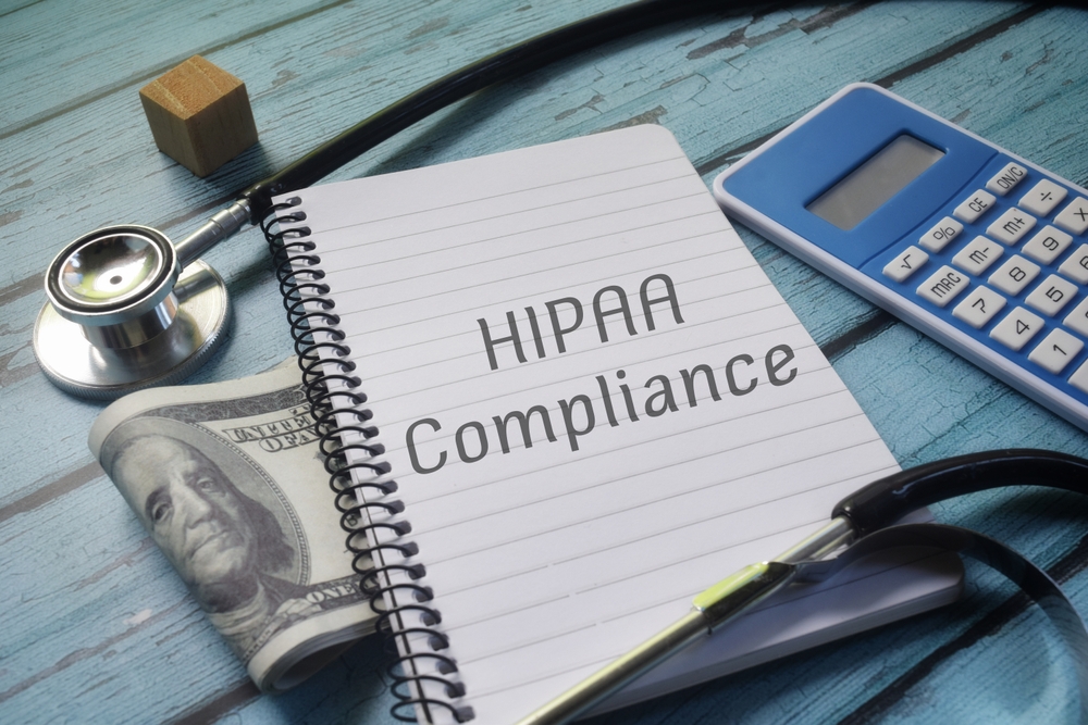 HIPAA compliance written on a notebook, with calculator money and stethoscope.