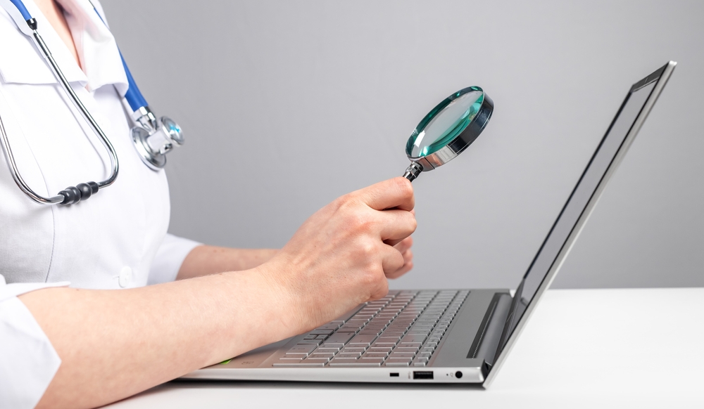 Virtual medical assistant holding magnifier over laptop screen.