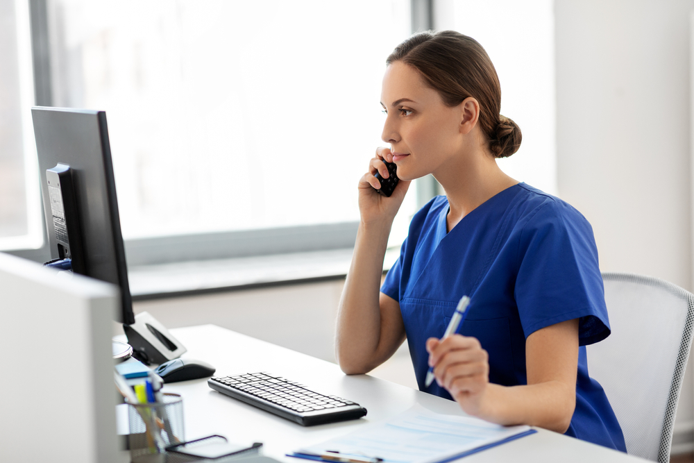 medical receptionist with computer and clipboard answering a phone call.