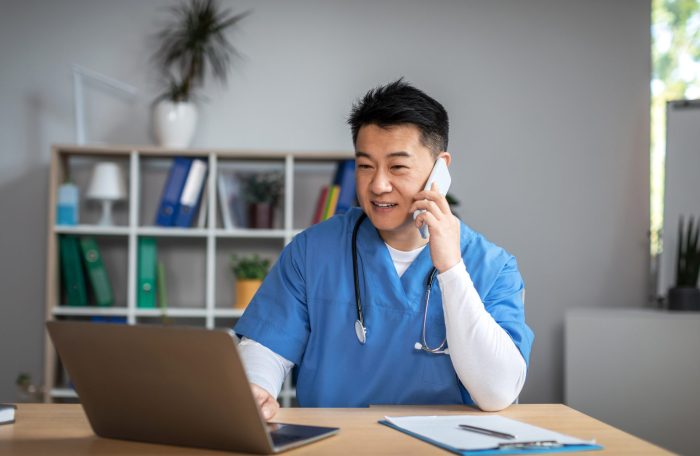 telehealth-ethical-practices-man-doctor-uniform-call-by-phone-types-computer-office-clinic-interior