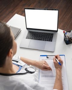 a female doctor writing on her clipboard and searching how become a virtual medical scribe on her laptop