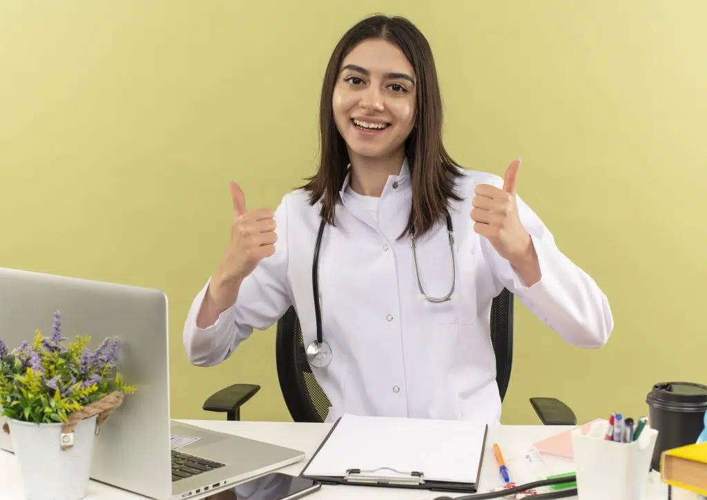 a young female doctor smiling cheerfully showing thumbs up sign representing "become a virtual medical scribe "