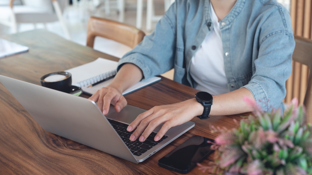 She types on her laptop while enjoying a coffe at her desk.