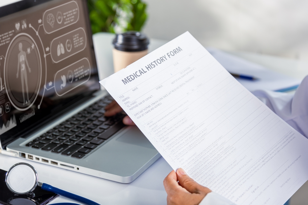 Typing information of patient prescription from paperwork medical history form into laptop computer for record document data report.