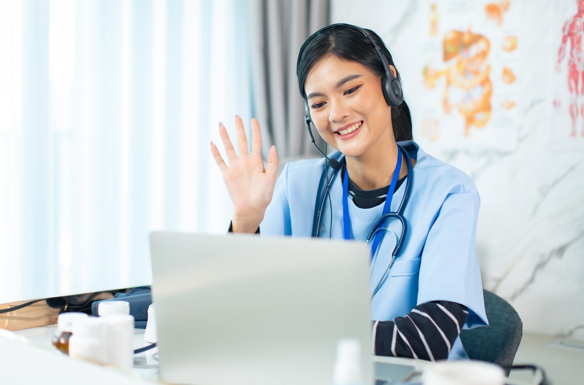 A female healthcare virtual assistants is waving while on her laptop.