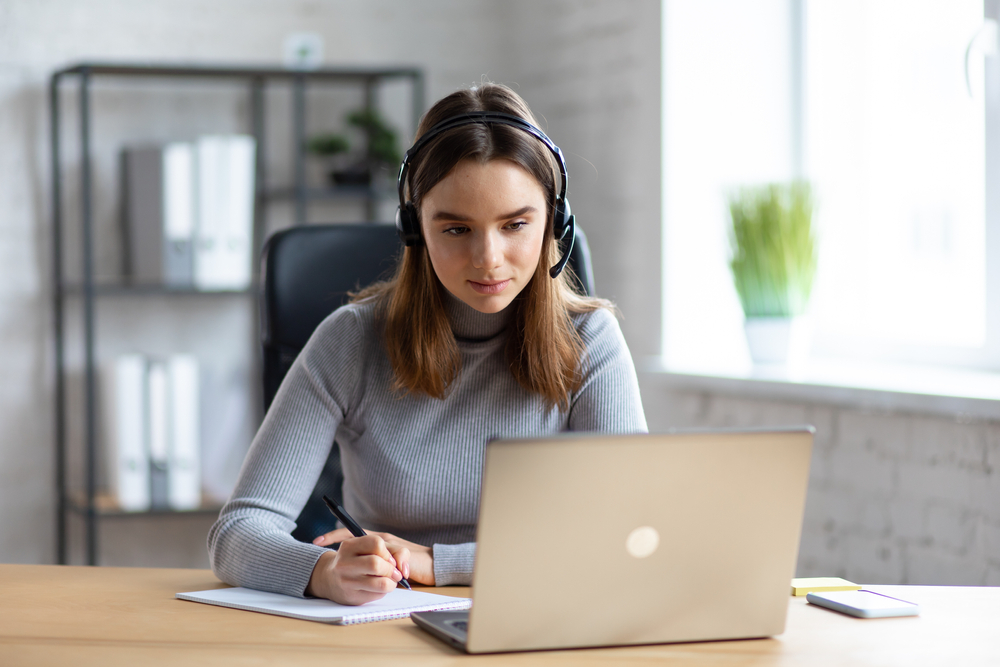 A skilled woman with a headset, laptop, and notebook delivers top-tier academic transcription services.
