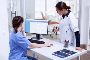 Stomatolog and nurse in tooth clinic checking patient appointment looking at computer monitor. Stomatology assistant and teeth doctor discussing in reception of dental office, dental office management 