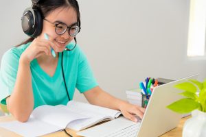 Asian young woman student with glasses headphones teenage girl study happy sitting looking video conference on a laptop computer, University class online internet learning distance education from home.