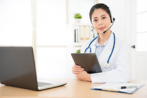 a doctor holding a clipboard while using her laptop