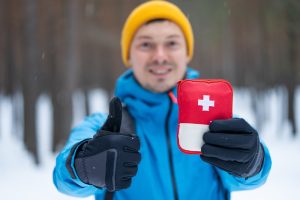 a man wearing winter clothing holding a medkit with a thumbs up.