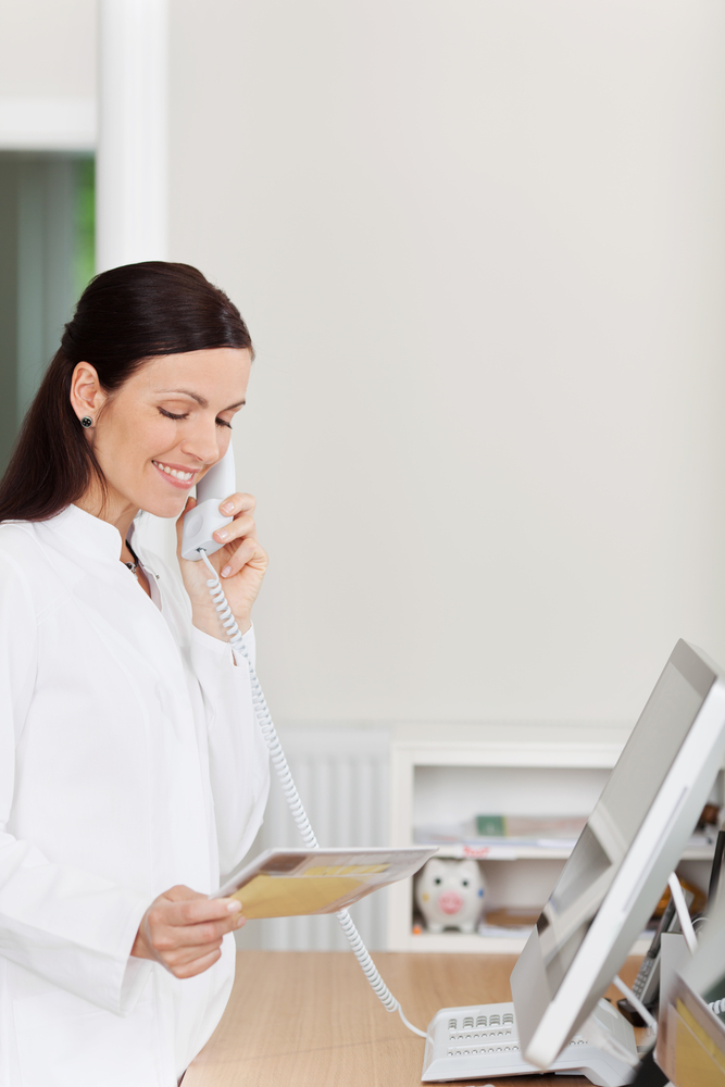 Female medical receptionist answers phone call at reception.