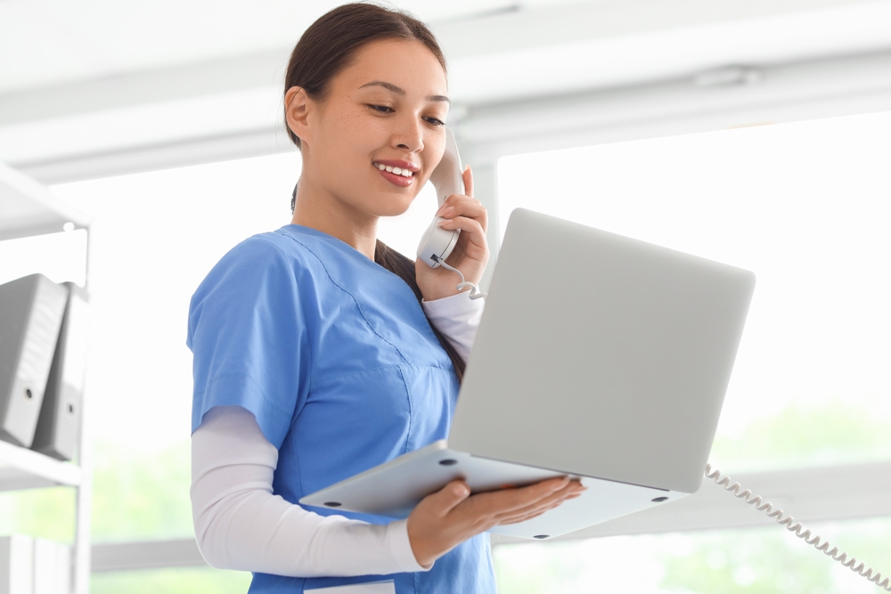 Female virtual medical phone operator holding a modern laptop while talking on the phone.