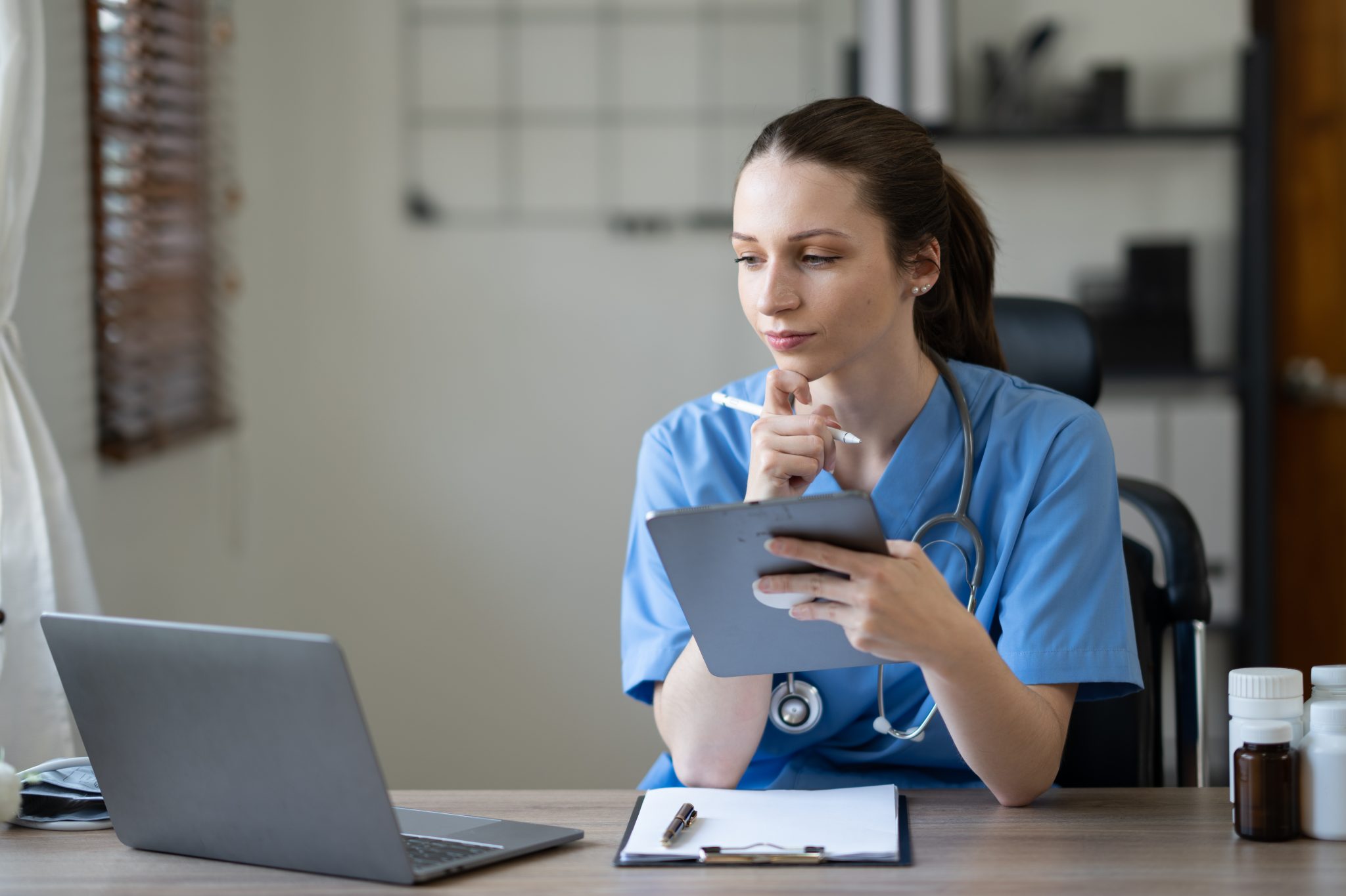 Virtual medical receptionist holding her tablet, while looking on her laptop. 