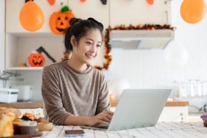 happy asian woman using her laptop, with a halloween background, halloween service receptionist