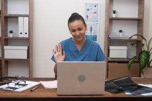 doctor in blue uniform welcoming patient in her laptop during an online consultation, emphasizing telemedicine, remote clinic management support