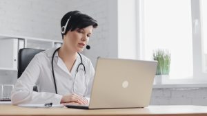 Female doctor consulting patient remote online using headset and web camera on laptop, virtual medical front desk staff