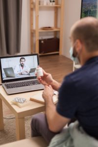 Guy in video conference with physician during self isolation sitting on sofa holding pills bottle,