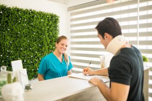 Therapist Looking At Athlete Filling Medical Form At Reception Counter, patient care receptionist