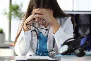 Close-up of tired medical worker working in cabinet. Big amount of patients. Exhausted young female doctor close head with hands. Medicine and healthcare concept, healthcare challenges receptionist