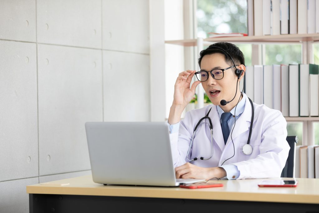 asian doctor talking with patient or co-worker through online video chat with computer in hospital, offshore medical customer service