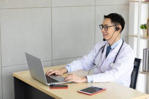 asian doctor talking with patient or co-worker through online video chat with computer in hospital, offshore medical customer service 