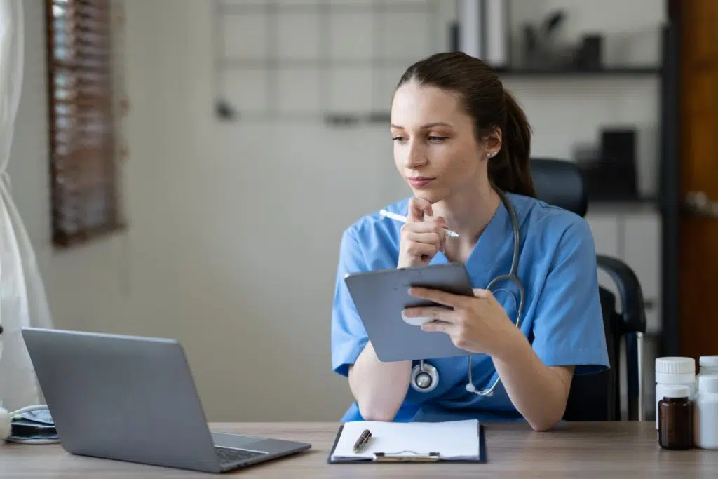 Female healthcare specialist holding a tablet and looking at her laptop on the table, searching how long does prior authorization take bcbs.