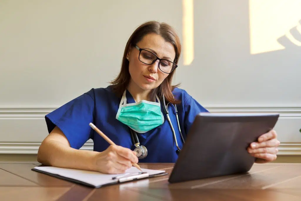Prior authorization specialist remote working holding a tablet while writing on a clipboard