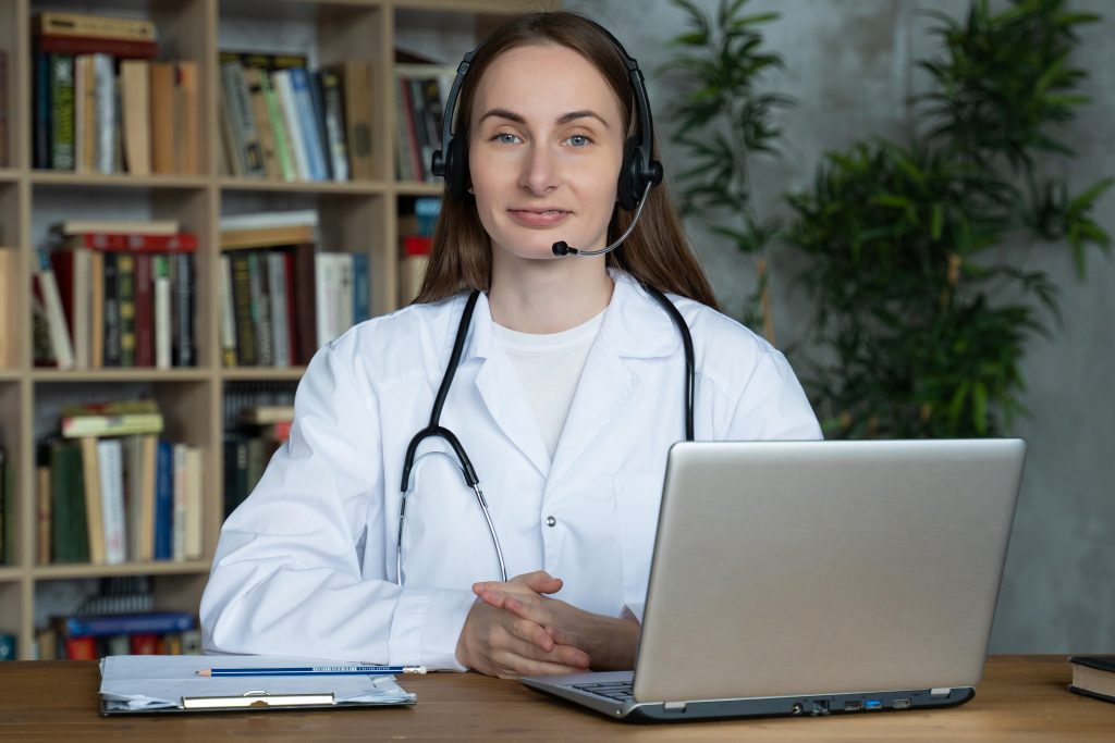 Virtual receptionist in healthcare wearing a headset consulting a patient through an online video call on a laptop screen