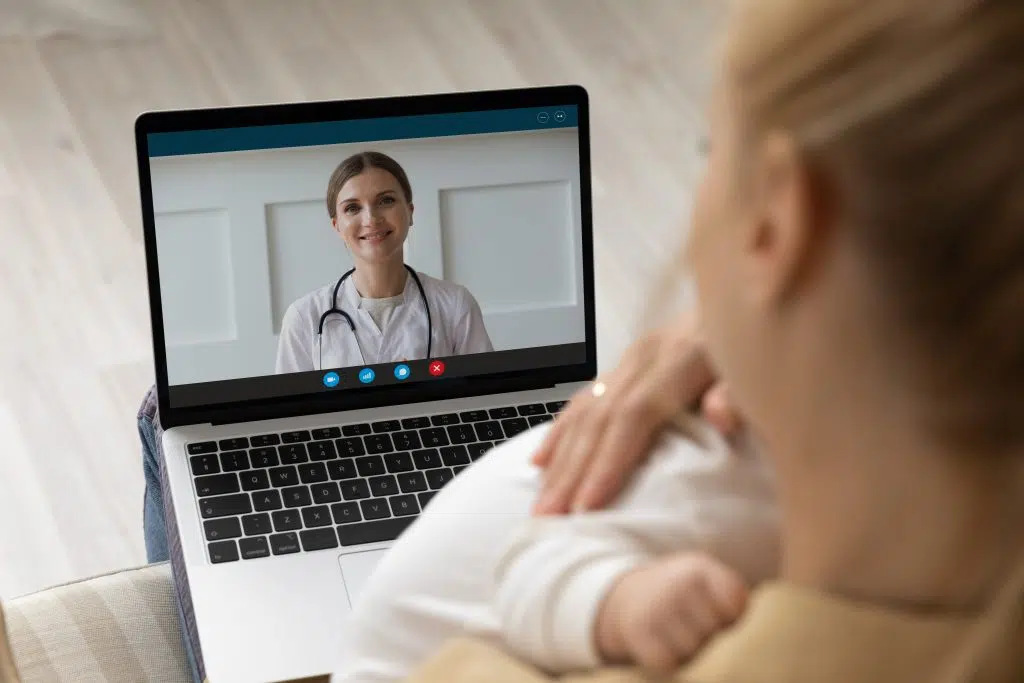 Close up over shoulder view of young Caucasian mother talk speak with doctor on computer on video call. Mom have webcam digital virtual online communication on laptop with family pediatrician, offshore patient follow-up services