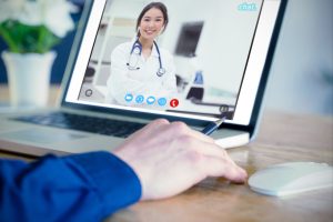 Businessman using laptop in office against pretty medical student smiling at camera, virtual clinic operations support