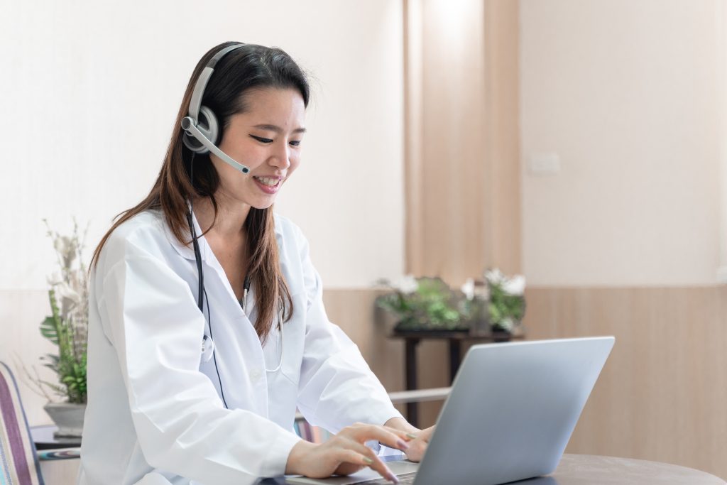 telemedicine concept, Asian woman doctor in headset taking calling on her headset microphone online for a ache patient, virtual clinic operations support