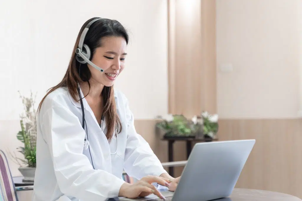 telemedicine concept, Asian woman doctor in headset taking calling on her headset microphone online for a ache patient, virtual clinic operations support