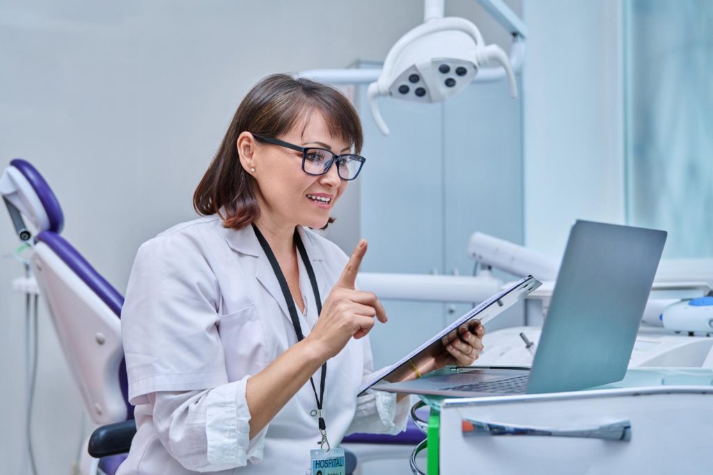 Dental virtual receptionist working in office on laptop and clipboard, making video call to consult with patients.