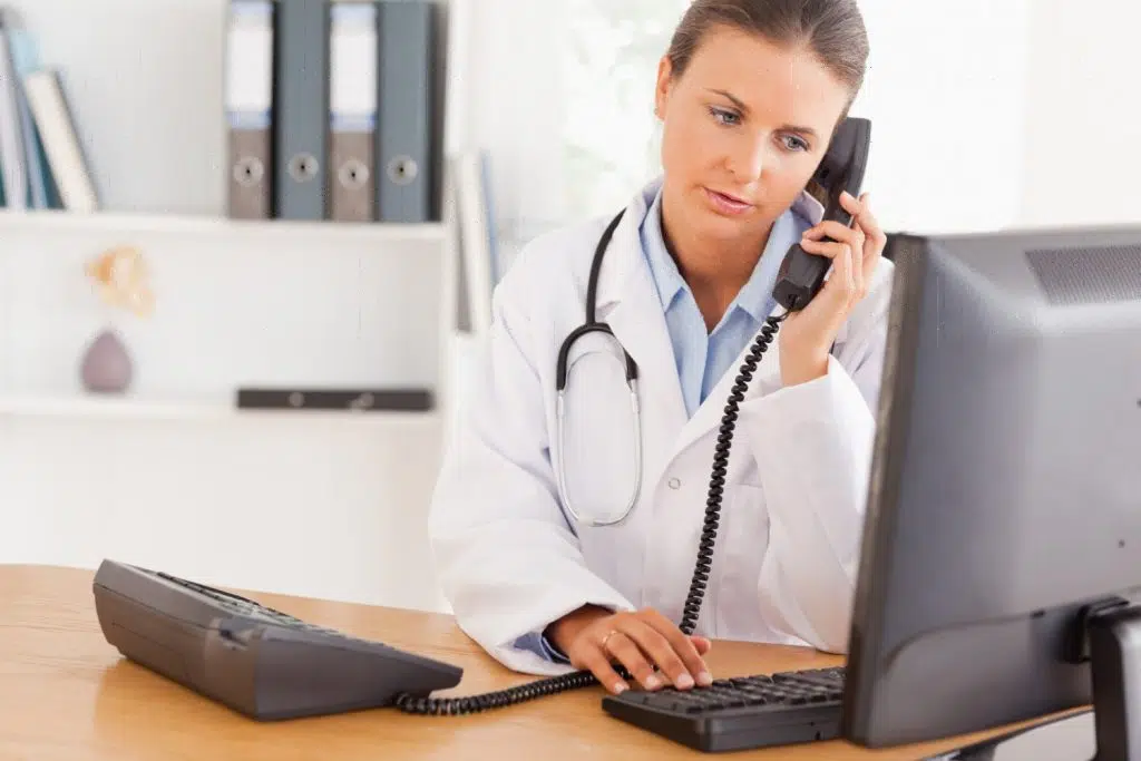 Digital medical receptionist speaking on the phone while working on a computer.