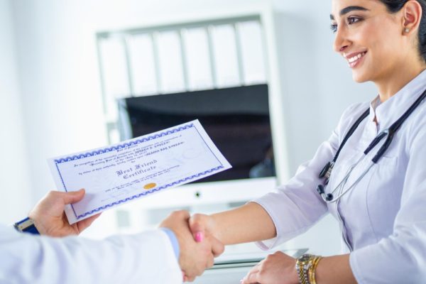 Doctor shaking hands while holding a certificate.