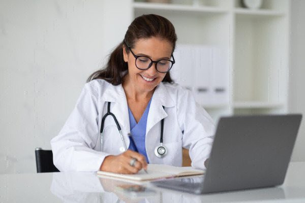Doctor sitting at desk using a laptop in a clinic.