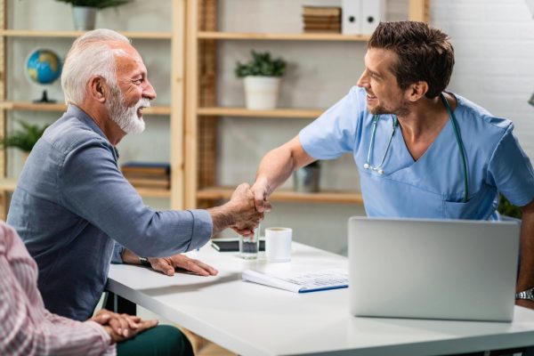 Happy doctor and mature man greeting and shaking hands during medical consultations