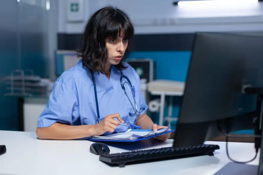Medical assistant working on a monitor while holding a clipboard for medical billing services for small practices