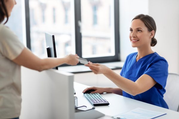 Medical receptionist assisting patient with credit card at hospital front desk.