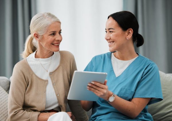 Patient care coordinator responsibilities with senior nurse consulting patient using tablet for healthcare reporting and medical assistance.